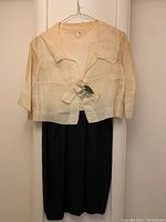 Front view of the vintage silk suit consisting of a cream cropped jacket hanging over black pants.