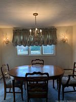 Wide angle photo showing the chandelier centered over a wooden dining table with two matching wall sconces on the adjacent walls.