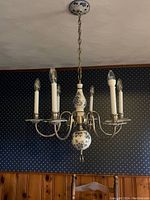 Chandelier hanging against a dark patterned wall above wood paneling, showing overall design, chain, and six bulbs.