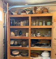 Wooden shelving unit filled with diverse kitchenware including glass jars, ceramics, metal items, and woven baskets.
