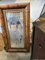 Front view of the large bamboo framed mirror resting against a wall, showing the full frame and mirror surface with some wear.