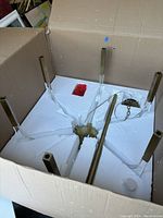 Chandelier components packed in cardboard box with protective Styrofoam inserts showing brass-finished iron supports and acrylic arms.
