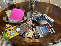 Full view of the items including notebooks, markers, glue tool, face paint palette, earbuds, clipboards, and postcard paper on round wooden table