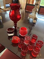 Red glass votive candle holders with various etched patterns and a tall red blown glass vase on a reflective surface.