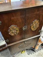 Front view of vintage wood radio cabinet showing double doors with decorative floral panels and brass hardware latch.