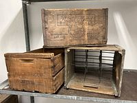 Three vintage wooden crates stacked on a metal shelf. One crate is open showing metal dividers inside.