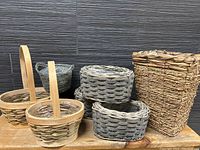 Seven assorted wicker baskets with liners, including two handled and five without handles, displayed against dark background.