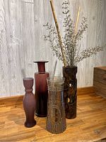 Four decorative glass vases arranged on wooden surface - three burgundy glass vases and one clear textured glass with wooden surround