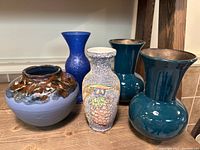 Lot of five decorative vases arranged together on wooden surface against wall.