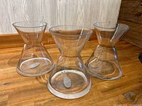 Three clear glass vases arranged side-by-side on wooden surface, showing their identical shape and size.