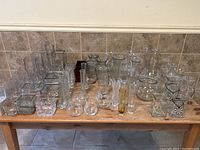 Front view of the assorted glass vases arranged on wooden table, visible variety of shapes, including square, round, cylindrical, and textured vases.