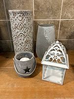 All four grey decorative items grouped on wood surface in front of tiled wall