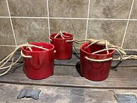 Three red ceramic hanging plant pots shown side by side with attached sisal rope hangers.