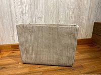 Front side view of a grey concrete rectangular planter with vertical ribbed design on wooden floor against light wood paneling wall.