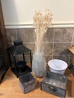 Wide view of the lot on a wooden surface including the vase with dried bunny tails, black tin lantern, white bucket, and metal containers.