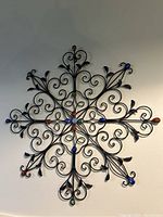 Full view of large circular metal wall art with black swirling and leaf details accented by colored glass orbs.
