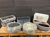 Front view of eight ceramic planters showing rectangular and oval shapes with various bark and stone-like textures in gray and beige tones.