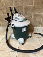 Shop Vac unit with hose and attached accessories on tiled floor background