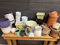 Large group of various small and medium new ceramic pots of different styles, colors, and shapes placed on wood bench against black wall
