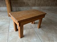 Small pine table viewed from an angle showing worn top surface and sturdy pine legs.