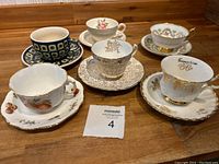 Overview image of 6 teacups and matching saucers, various patterns and styles displayed on wooden surface