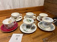 Full set of 6 teacups with matching saucers displayed on wooden surface showing their varied floral and emblem designs
