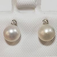 Front view of pair of stud earrings with white fresh water pearls and small diamonds in 14K gold settings on display holder.