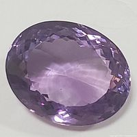 Close-up photo of the oval cut genuine amethyst gemstone showing its color and faceted surface.