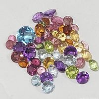 Various loose faceted gemstones in multiple colors and shapes arranged on white background.