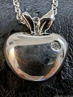Close-up of polished rhodium-plated sterling silver apple-shaped pendant with diamond accent, showing smooth reflective surface and pendant bail.