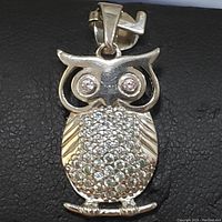 Top view of the sterling silver owl pendant showing the cubic zirconia stones on the eyes and the pavé-set stones on the body. The owl is perched on a small branch detail at the bottom.