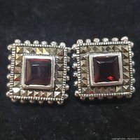 Close-up frontal view of the square sterling silver earring with central garnet and surrounding marcasite stones on black background.
