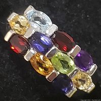 Close-up of ring showing faceted colorful gemstones in rows with silver prong settings