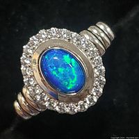 Close-up view of sterling silver ring showing oval blue opalite center stone with surrounding clear cubic zirconia stones and band detail.