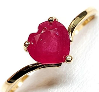 Close-up of ring face showing heart-shaped ruby prong set on yellow gold bypass shank against white background