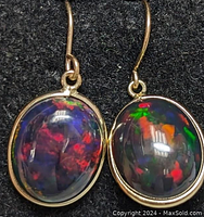 Close-up photo of earrings showing black opal cabochons set in 14K yellow gold bezels with ear wires.