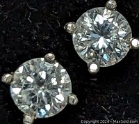 Close-up of two 14K white gold diamond stud earrings showing the clear round-cut diamonds in four-prong settings on black background.