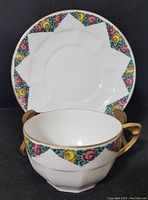 Teacup and saucer set with floral and geometric border, gold handle on the teacup, showing the front view.