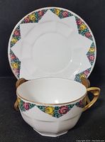 Front view of teacup in front of saucer showing floral border and gold-tone handles.