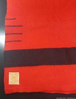 Close-up of corner showing red fabric with black stripes and small woven label with Hudson's Bay mark.