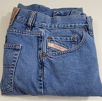 Folded front view of blue denim jeans showing Diesel Industry label on coin pocket and belt loops.
