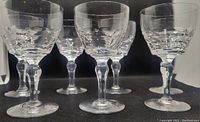 Seven clear crystal wine goblets with Chippendale cut pattern, arranged in a row against black background.