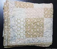 Folded view of the handcrafted quilt showing earthtone fabric patches including florals and geometric patterns.