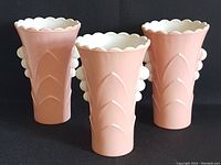 Front view of three pink on white Fire King Vitrock vases with scalloped rims and Art Deco floral motifs