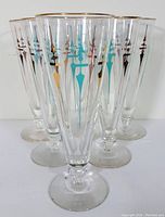 Six vintage Libbey Staccato pilsner glasses with multicolor vertical geometric pattern and gold rims, arranged in a group.