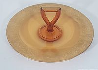 Full view of amber glass serving plate with central handle and detailed golden pattern around the rim.