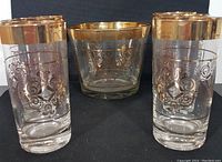 Set of one glass ice bucket and six glasses arranged on a dark background, showing golden decorative accents and symmetrical patterns on glassware.