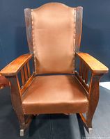 Front view of antique oak mission style rocking chair with brown leather upholstery and stud detail