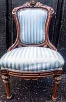 Front view of antique arm chair showing striped blue upholstery and carved wooden frame