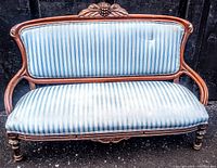 Front view of antique settee showing hand carved wooden frame and blue and white striped upholstered cushions with tufted detail.